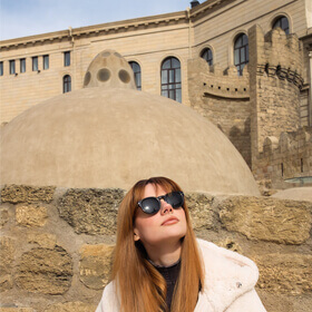 Woman standing outside Haji Gayib Bathhouse in Baku Old City with the historic dome behind